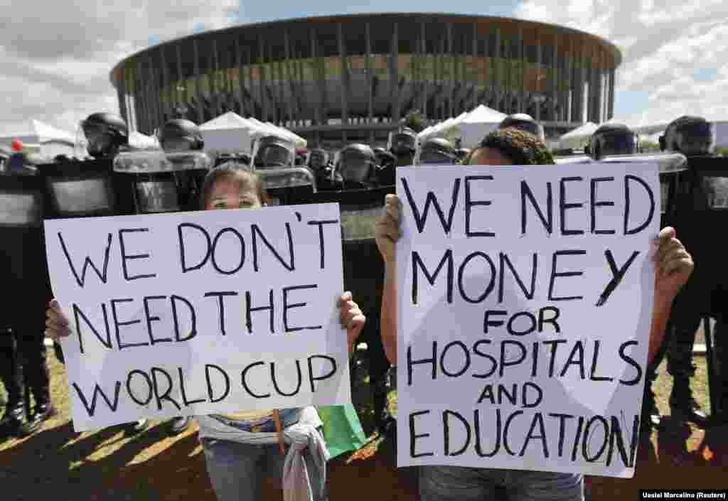 Brasileiros exibem cartazes dizendo que não precisam do mundial, à esquerda, e "Precisamos de dinheiro para os hospitais e para a Educação, à direita.