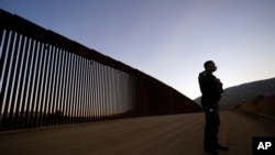 FILE - Border Patrol agent Justin Castrejon stands in front of newly replaced border wall sections, near Tecate, California, Sept. 24, 2020.