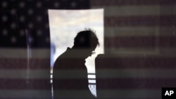 FILE - A voter is reflected in an image of a U.S. flag, as he casts his ballot on Election Day in Jamul, California, Nov. 6, 2012. 