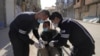 Health workers put gloves on a man in a wheelchair on an empty street, as restrictions are imposed to prevent the spread of the coronavirus in Qamishli, Syria, March 23, 2020. 