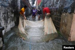 FILE - Men use a mosquito net to catch fish in a flooded alley in a residential district in Bacoor, near Manila, Phillippines, Aug. 20, 2013.