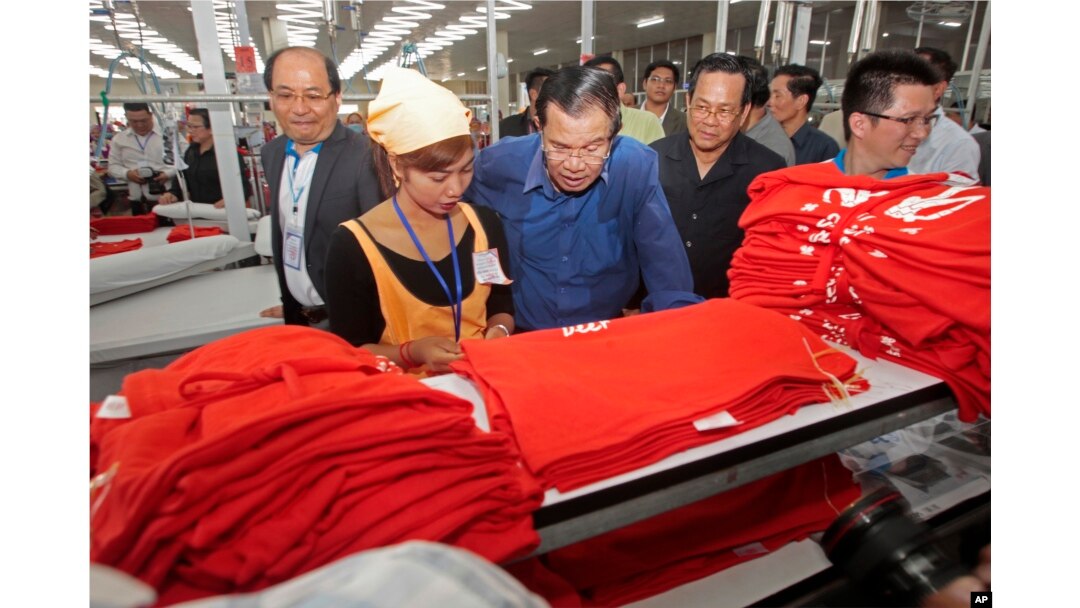 FILE - Prime Minister Hun Sen, center, leans over a garment worker during a visit to a factory outside Phnom Penh, Cambodia, Aug. 30, 2017.