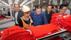 FILE - Prime Minister Hun Sen, center, leans over a garment worker during a visit to a factory outside Phnom Penh, Cambodia, Aug. 30, 2017.
