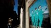 FILE - A woman wearing a protective face mask walks past a painting representing Moderna, Pfizer and AstraZeneca vaccines at Bisbe street, during the COVID-19 outbreak, in Barcelona, Spain, Jan. 27, 2021.