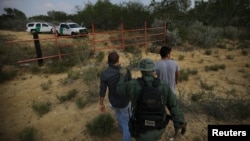 FILE - A U.S. border patrol agent escorts men being detained after entering the United States by crossing the Rio Grande River from Mexico, in Roma, Texas, May 11, 2017.