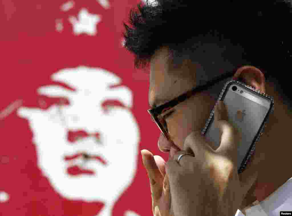 有中国人用苹果手机打电话,旁边是雷锋画像(2013年)。中国青年热衷于iPhone,而不是雷锋。而中国当局谨防iPhone之类的上网工具带来“西风”——来自西方和海外的对当局不利的信息和影响,也希望让其1960年代的洗脑工具雷锋成为人们学习的榜样。