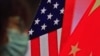 资料照：一名戴口罩妇女坐在显示美中国旗的屏幕前