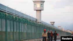 中国新疆维吾尔自治区达坂城的官方所谓的职业技能教育中心的围栏旁边，有工人走过。(2018年9月4日)