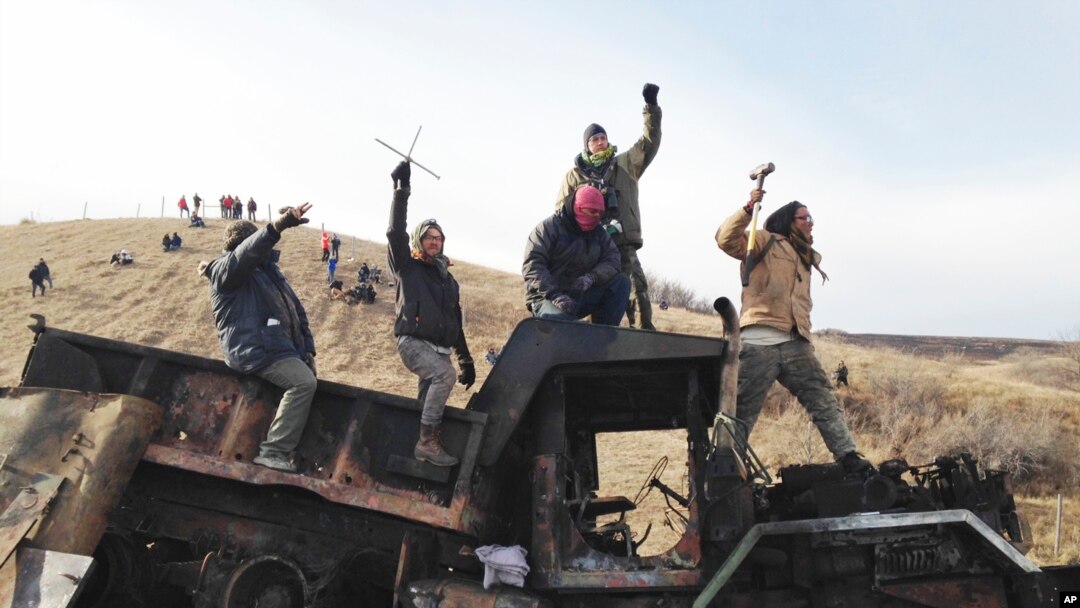  FILE - Protesters against the Dakota Access oil pipeline stand on a burned-out truck near Cannon Ball, N.D., that they removed from a long-closed bridge near their camp in North Dakota, Monday, Nov. 21, 2016. 
