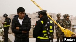 在中國新疆維吾爾自治區喀什的一條街上，警察檢查一名男子的身份證，旁邊有安全人員（2017年3月24日）