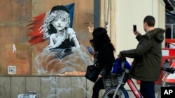 Commuters take photos on their phones of a new artwork by British artist Banksy, opposite the French Embassy, in London, Monday, Jan. 25, 2016. 