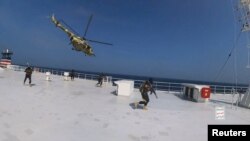 Houthi military helicopter hovers over the Galaxy Leader cargo ship as Houthi fighters walk on the ship's deck in the Red Sea