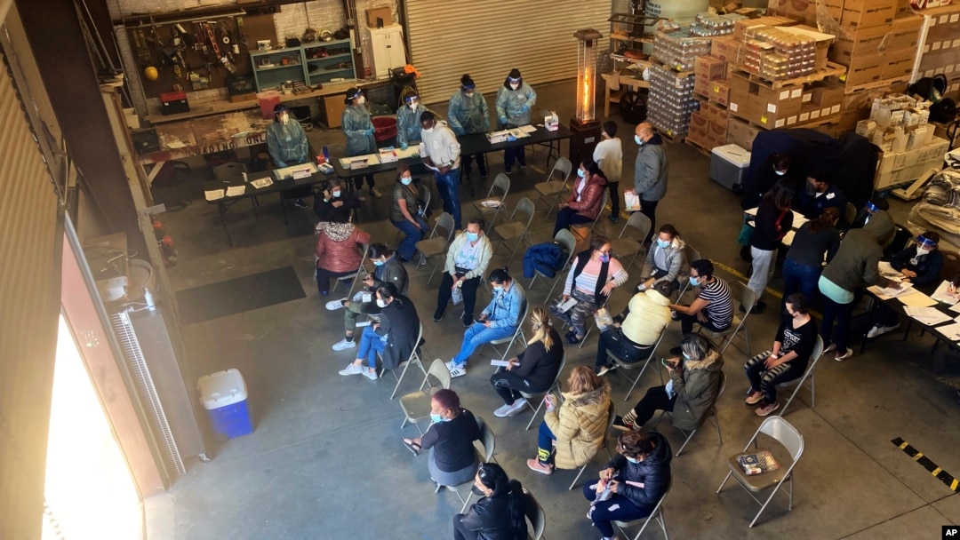 FILE - Migrants released by the Border Patrol with notices to appear in court, Feb. 5, 2022, in Somerton, Ariz., wait for COVID-19 testing at a Regional Center for Border Health warehouse.