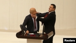 Turkey's AKP party lawmaker Alpay Ozalan, right, scuffles with Workers' Party of Turkey lawmaker Ahmet Sik, who was speaking during the Turkish parliament's meeting to discuss jailed opposition lawmaker Can Atalay's return to the assembly, in Ankara, Turkey, on Aug. 16, 2024.