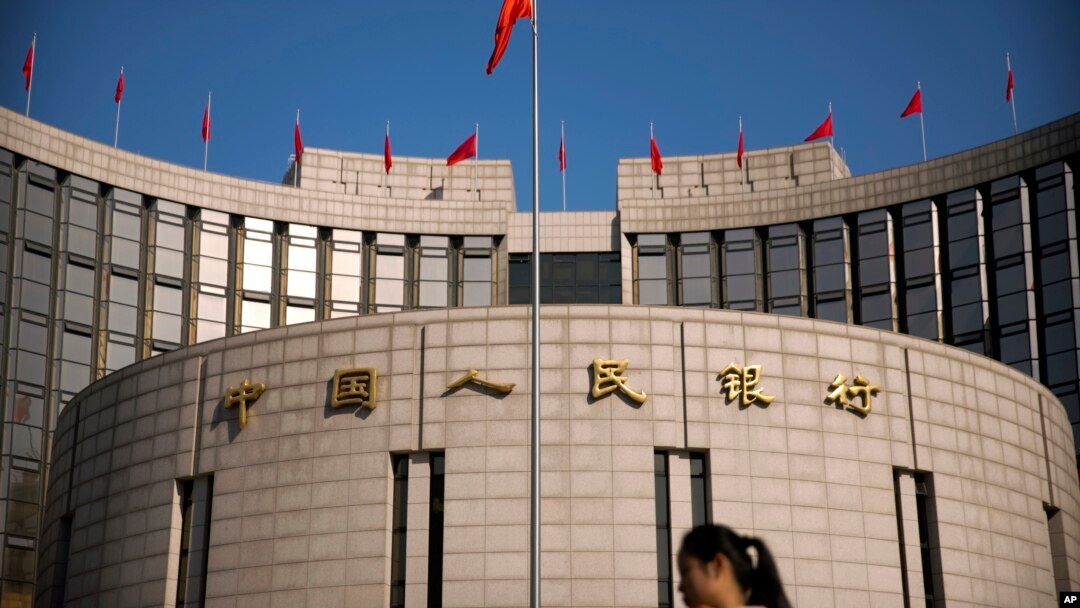 FILE - In this March 10, 2017, file photo, a woman walks past the headquarters of the People's Bank of China in Beijing. China’s central bank is planning to issue digital currency with tracking controls it will supervise.