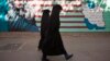 FILE - Iranian women walk past an anti-U.S. mural on the wall of the former U.S. embassy in Tehran, Oct. 12, 2011. 