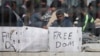 Seen through a wire fence, refugees and migrants most of them from Pakistan, hold placards during a third day of hunger strike to protest their deportation to Turkey, in the Greek island of Lesbos, April 7, 2016. 