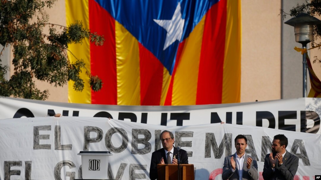 Catalan regional President Quim Torra, centre, applauds in front of a large Catalonia independence flag during a rally in Sant Julia de Ramis, Spain, Oct. 1, 2018.