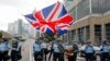 FILE - A woman waves a British flag as policemen in anti-riot gear stand guard against protesters on a closed-off road near the Legislative Council in Hong Kong, June 12, 2019.