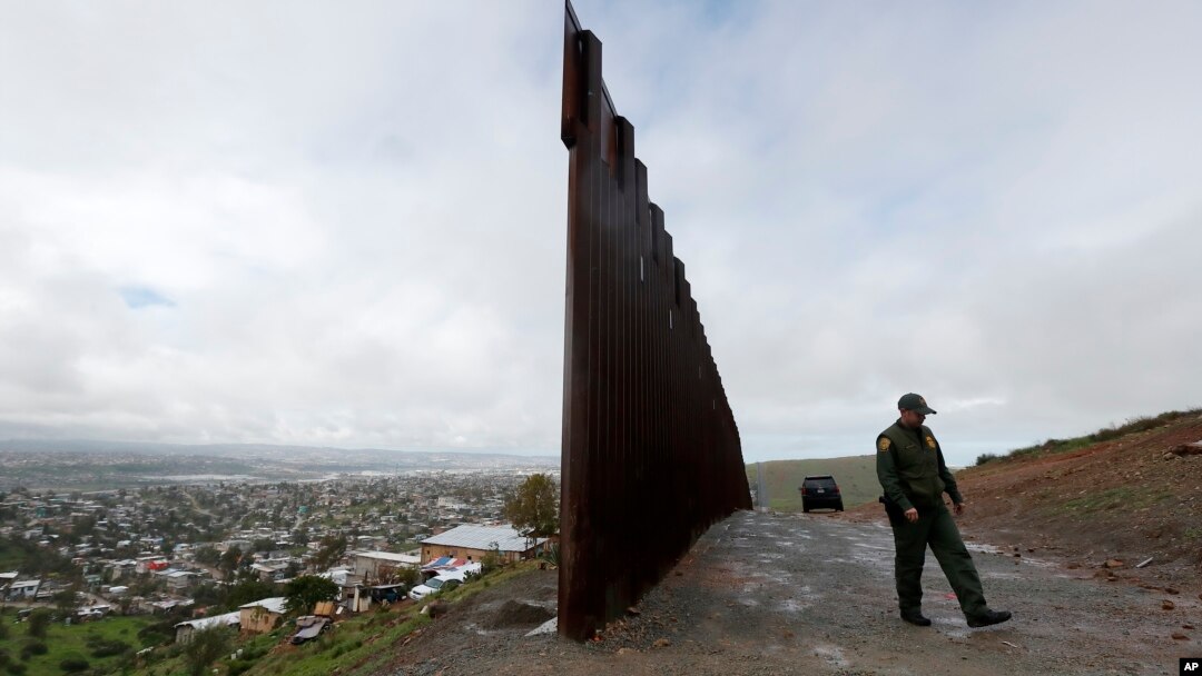 FILE - A Border Patrol agent walks near where the border wall ends that separates Tijuana, Mexico, left, from San Diego, right, Feb. 5, 2019.