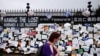 A woman passes a fence outside Brooklyn's Green-Wood Cemetery adorned with tributes to victims of COVID-19, Thursday, May 28, 2020, in New York. The memorial is part of the Naming the Lost project which attempts to humanize the victims who are often…